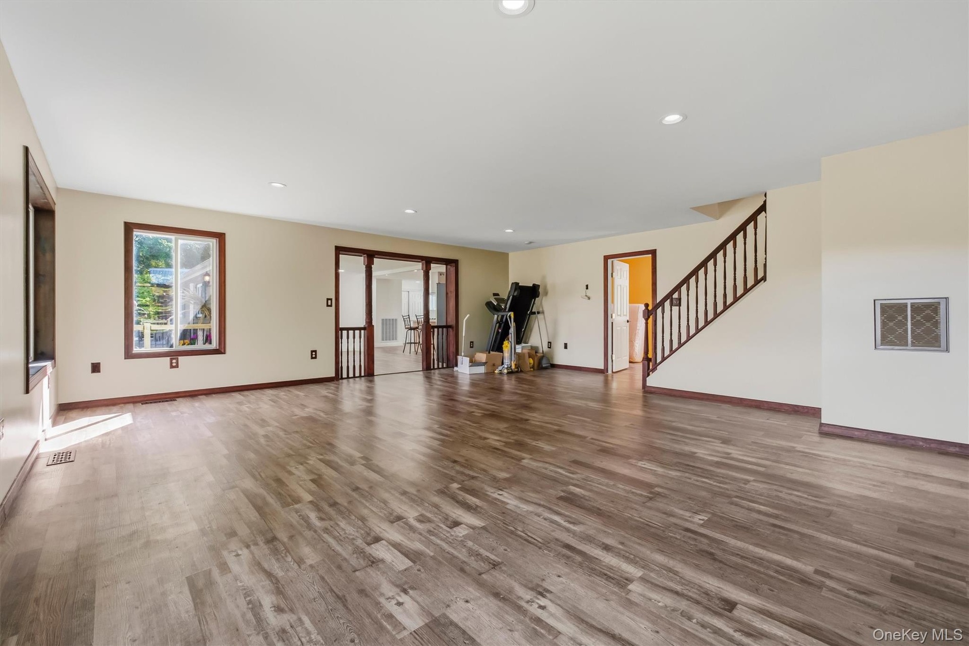 Spacious livingroom featuring wood-finish flooring, recessed lighting, and a prominent staircase with dark wood railings