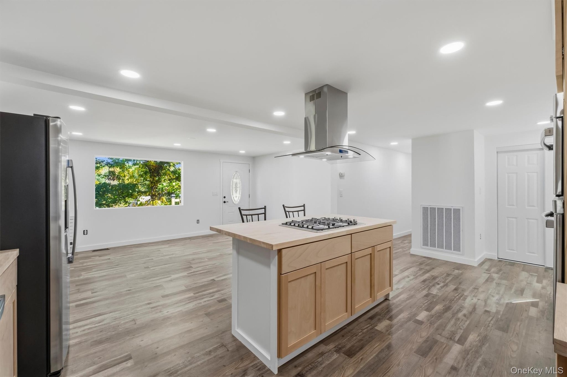Kitchen island with a built-in gas cooktop, stainless steel range hood, wood-finish flooring, recessed lighting, and white walls