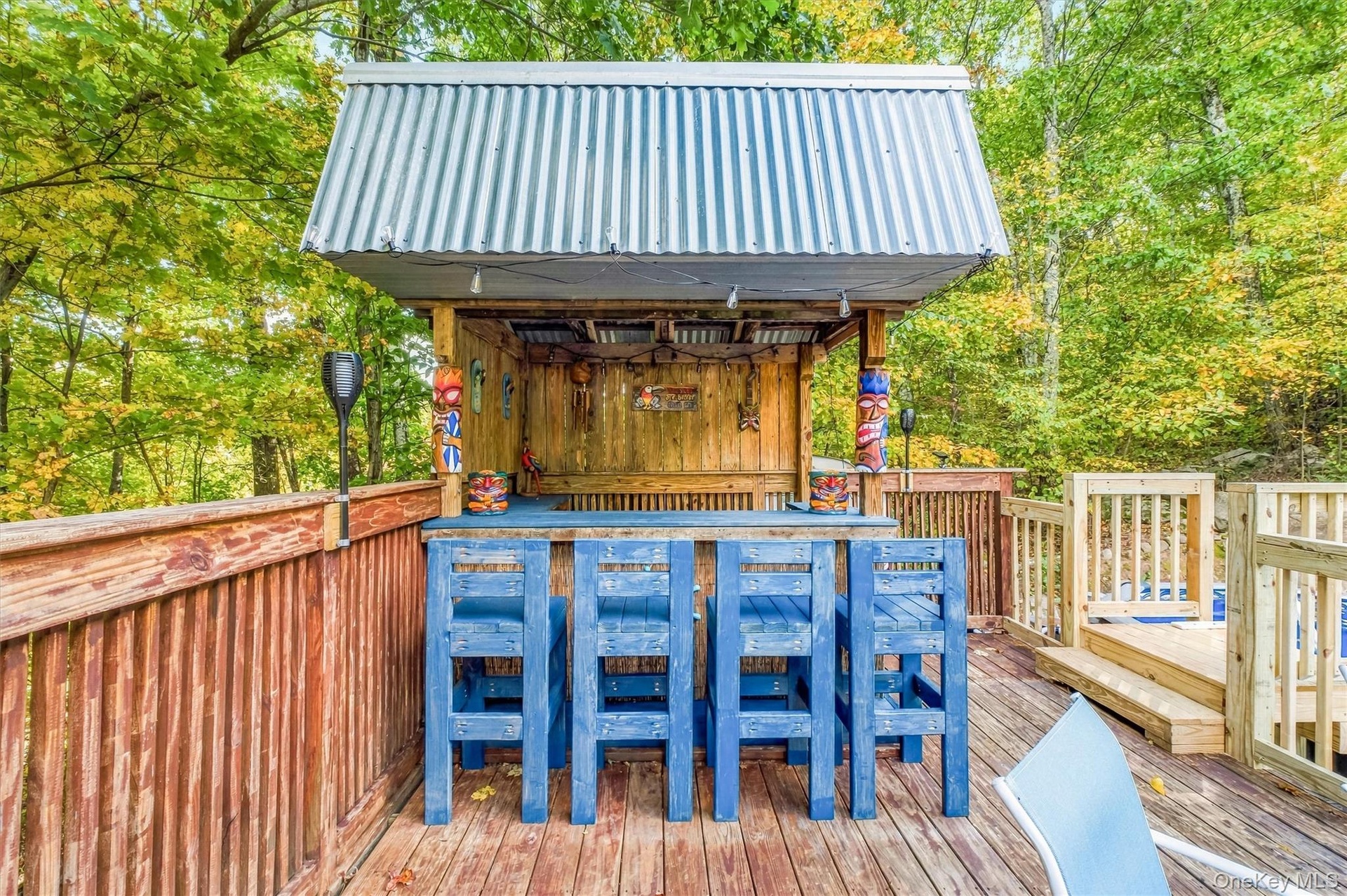 Outdoor bar structure featuring a corrugated metal roof, wood construction, and a bar counter with seating