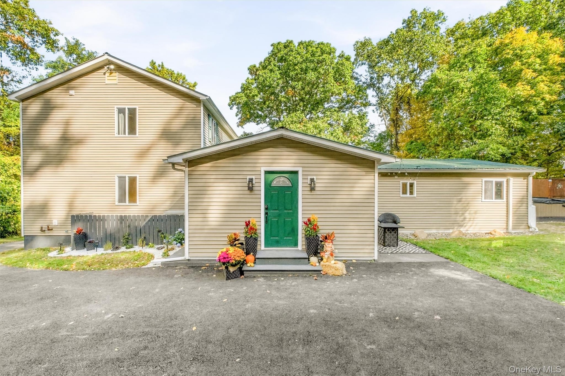 Rear view of home featuring neutral-toned siding, a vibrant green entry door, and a paved driveway