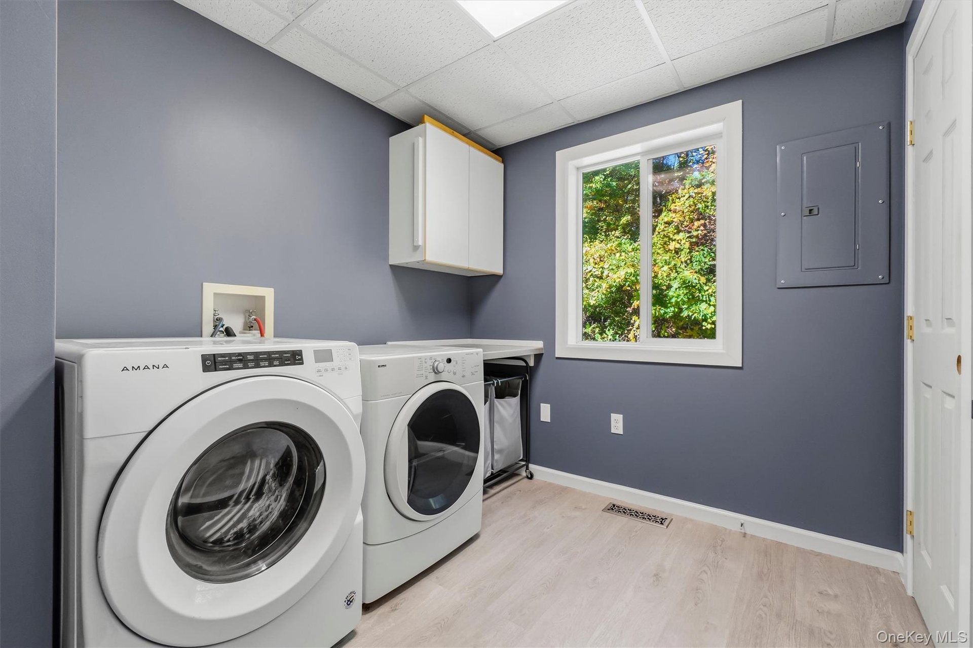 Spacious laundry room featuring wood-finish flooring, white cabinetry, a large window, and a built-in folding counter