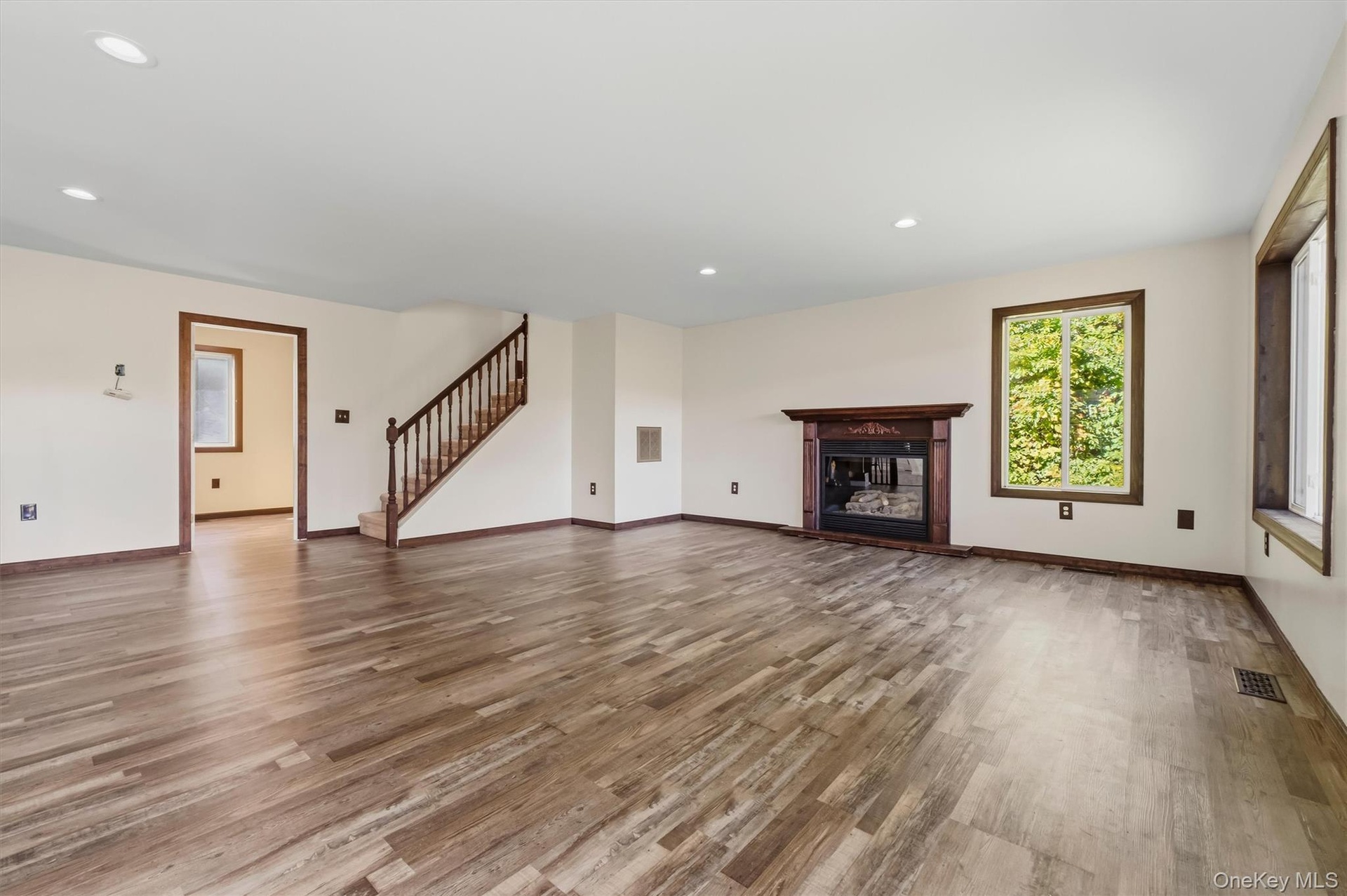 Recessed ceiling lighting, wood-finish flooring, dark wood trim, fireplace with dark wood mantel, and a staircase with wood railing