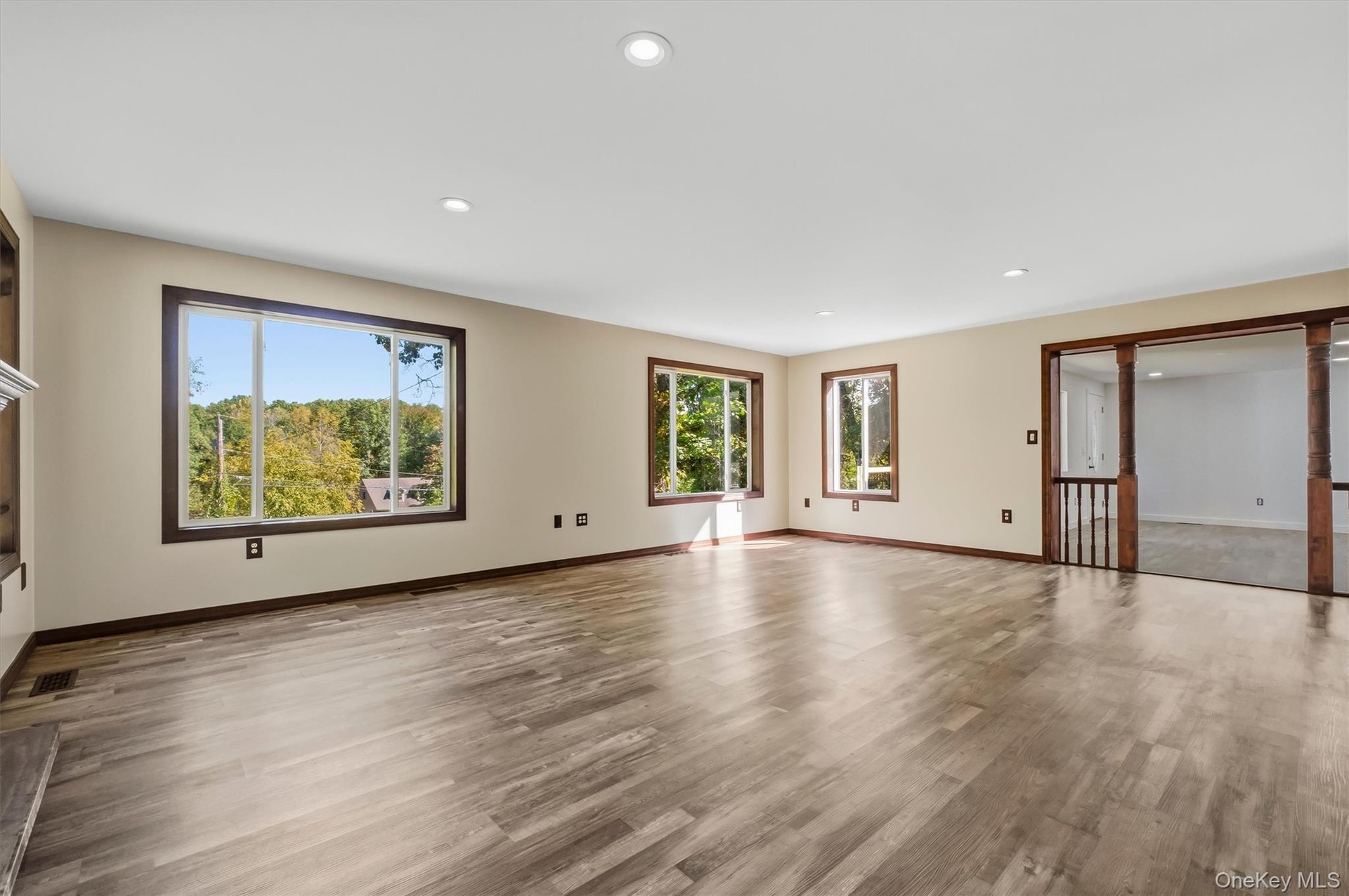 Recessed lighting, wood-finish flooring, multiple windows with dark wood trim, and a built-in fireplace mantle