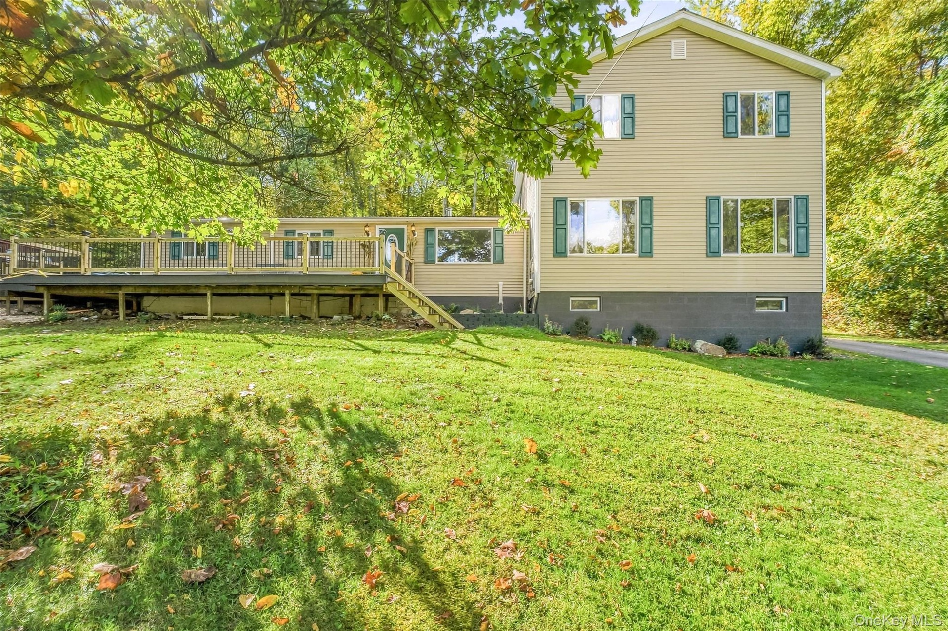 Spacious exterior deck with wood railing, set against a backdrop of mature trees and a manicured lawn