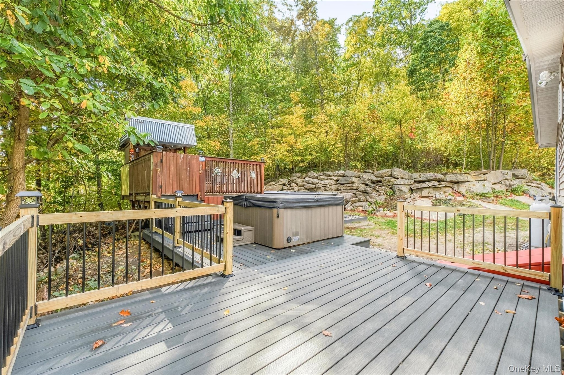 Expansive outdoor deck featuring composite decking, wood railings with black balusters, a built-in hot tub, and a multi-level play structure