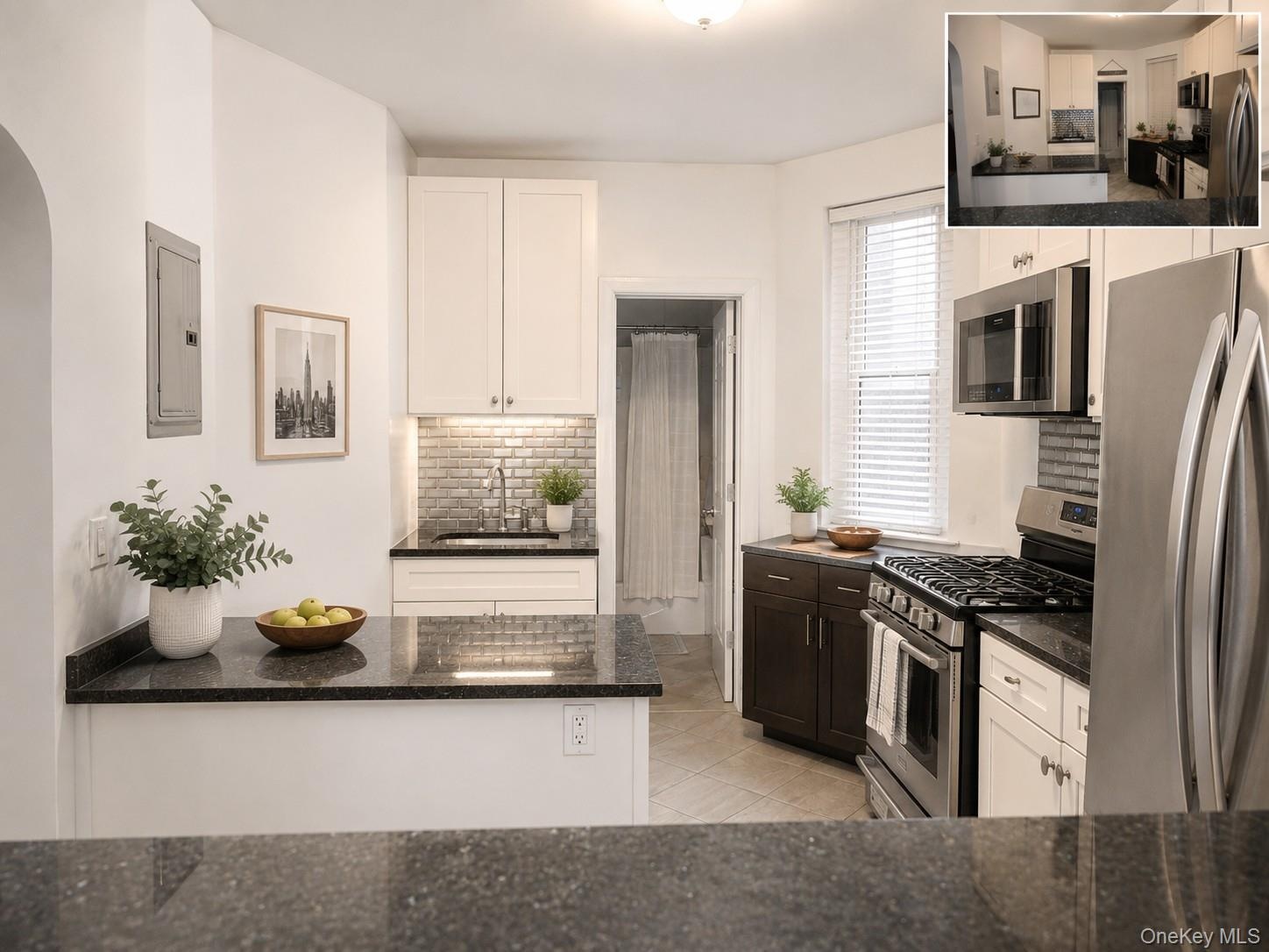 Contemporary kitchen featuring black granite countertops, white cabinetry, and stainless steel appliances (virtually staged)