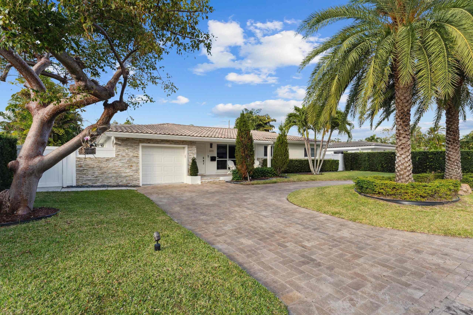 Elegant single-story residence featuring a stone and stucco exterior, wide circular driveway with paver construction, mature landscaping including a s
