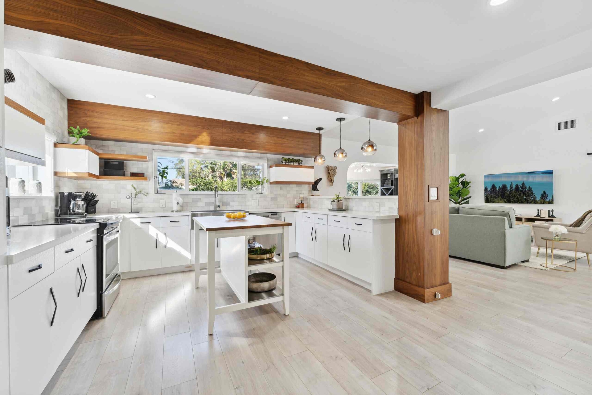 Contemporary kitchen and open-concept living space featuring white cabinetry with hardware accents, a large center island with open shelving, and stai