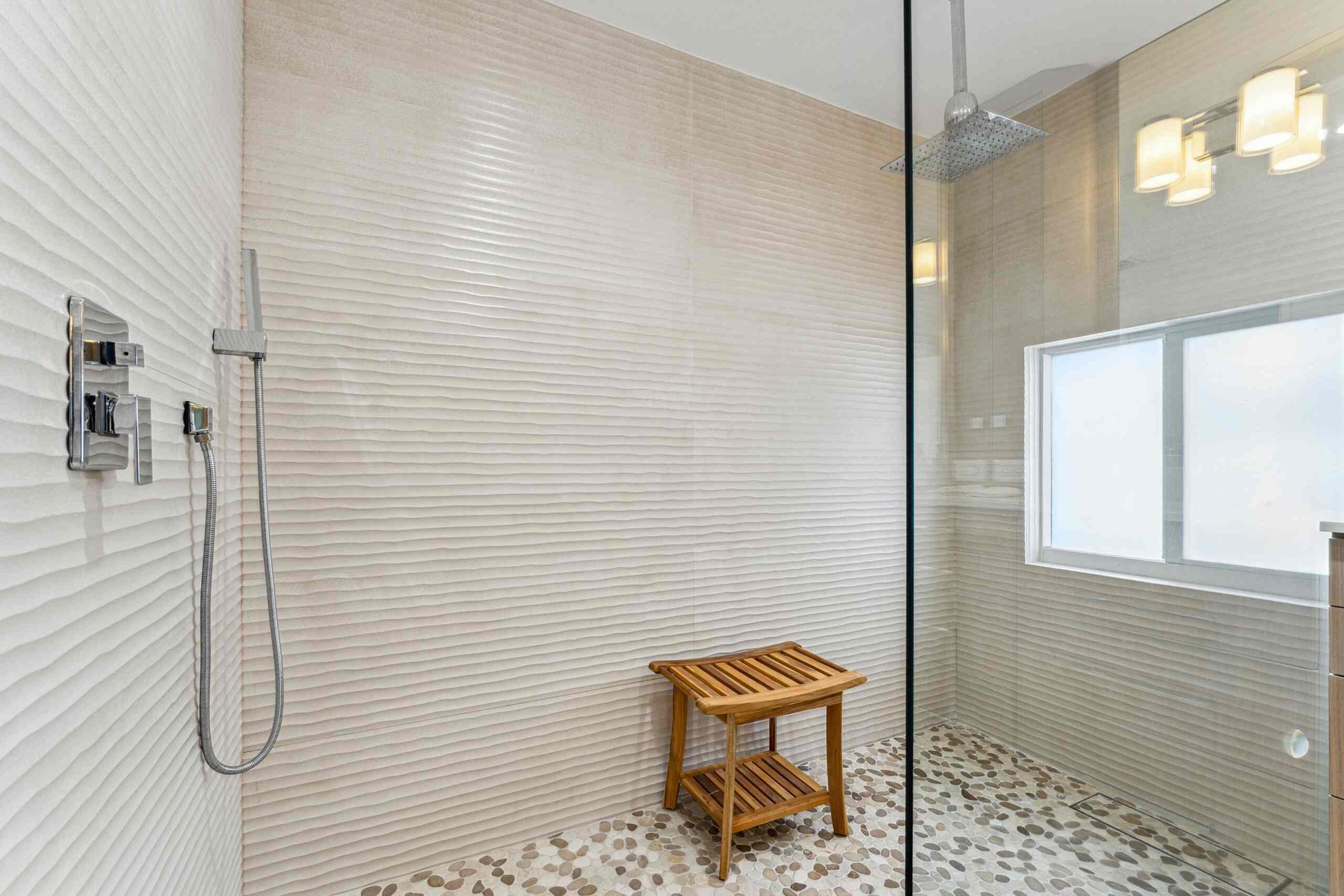 Walk-in shower featuring textured wall tiling, a rainfall showerhead, a hand-held shower fixture, and pebble-finish flooring