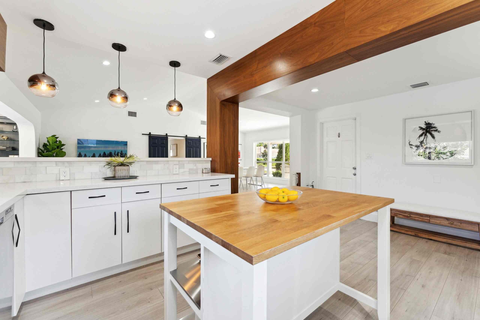 Modern kitchen featuring white cabinetry, a substantial wood-topped island with storage, pendant lighting with copper-finish shades, and a large wood 