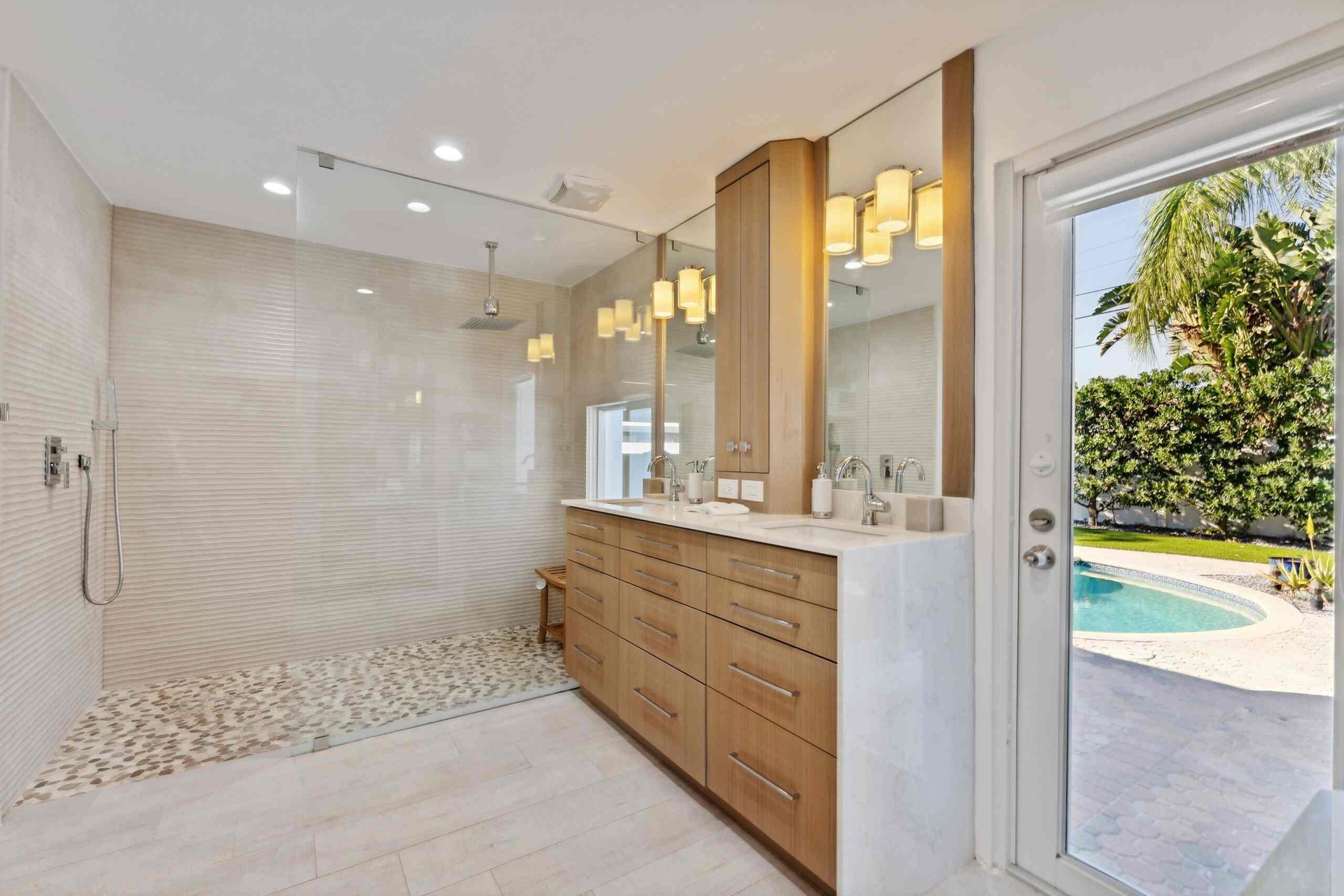 Spa-inspired primary bathroom featuring a spacious walk-in shower with white subway tile surround and pebble stone flooring, custom wood-finish vanity