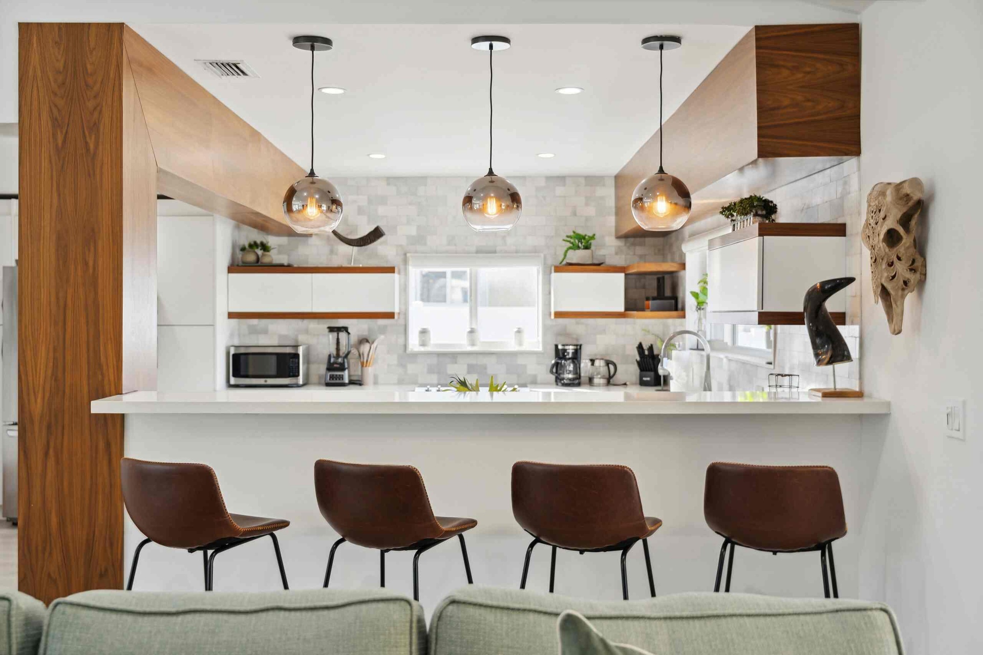 Kitchen featuring a white countertop island with integrated seating, three pendant lights, wood-finish beams, white cabinetry with wood-finish accents