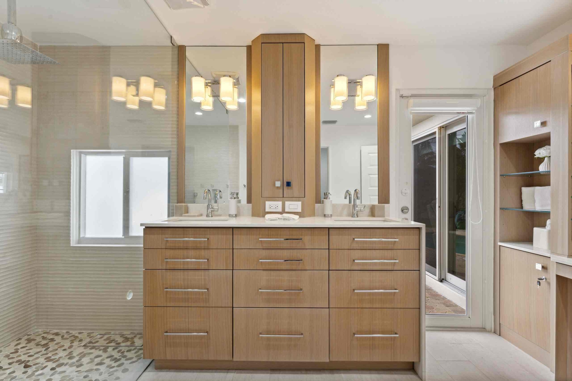 Spa-inspired primary bathroom featuring a custom wood-finish double vanity with dual sinks, polished nickel hardware, and an illuminated mirror surrou