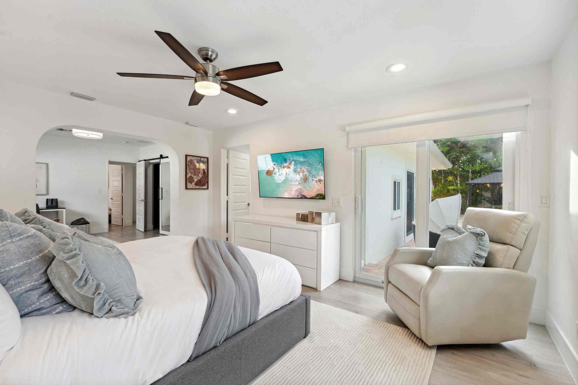 Spacious primary bedroom suite featuring a gray upholstered bed frame, ceiling fan with integrated lighting, ensuite bathroom access, and a comfortabl