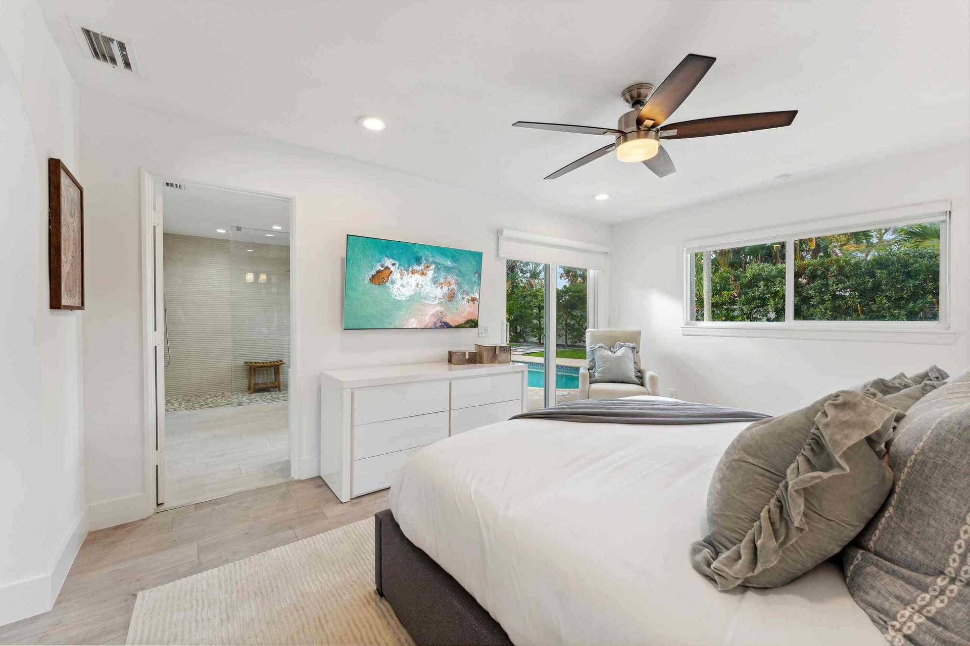 Bright primary bedroom featuring a wood-finish plank floor, ceiling fan with integrated lighting, and abundant natural light from dual windows