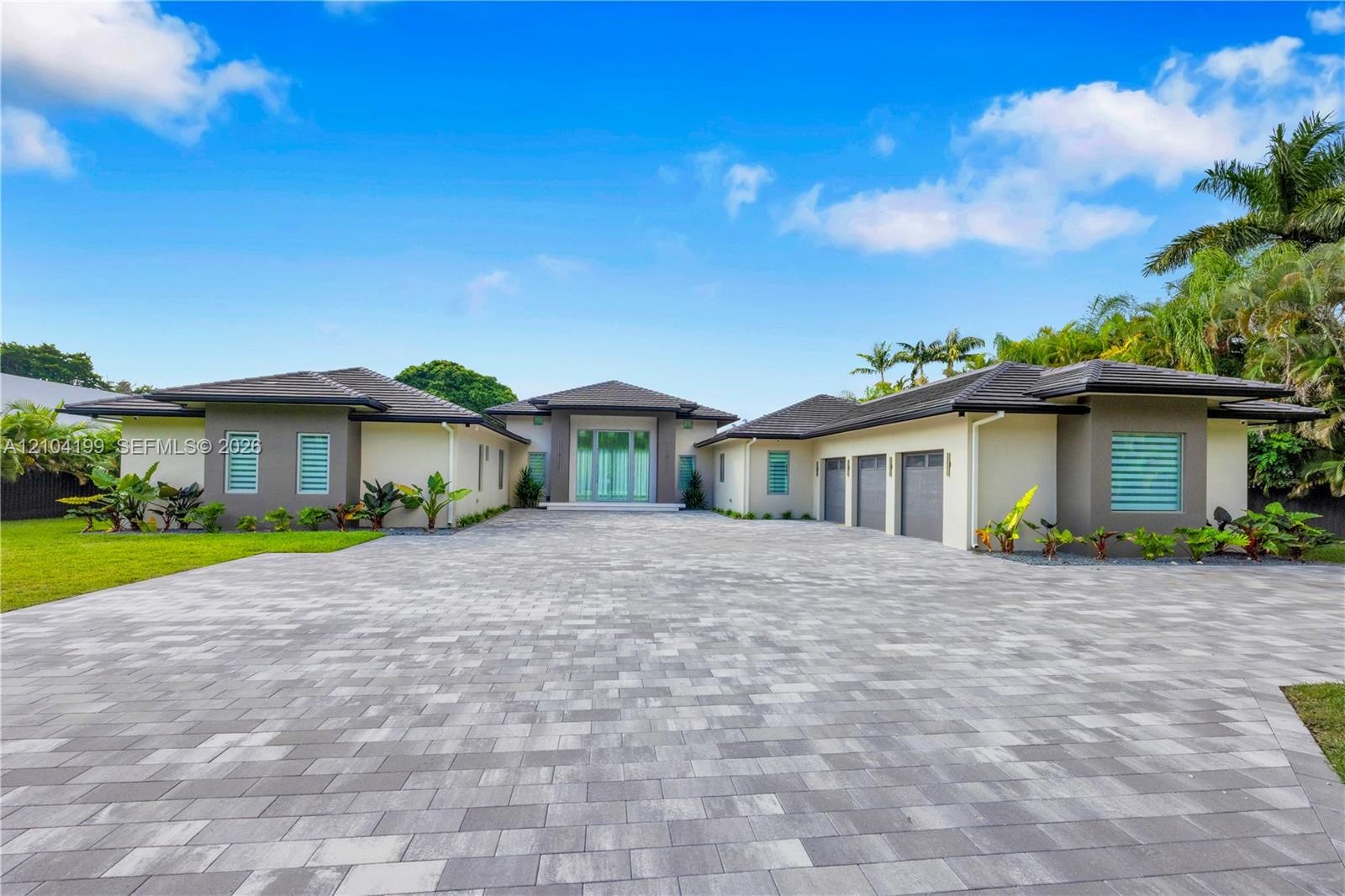 Paver stone driveway featuring an gated entrance with vertical fencing, mature palm trees, and wall-mounted exterior lighting