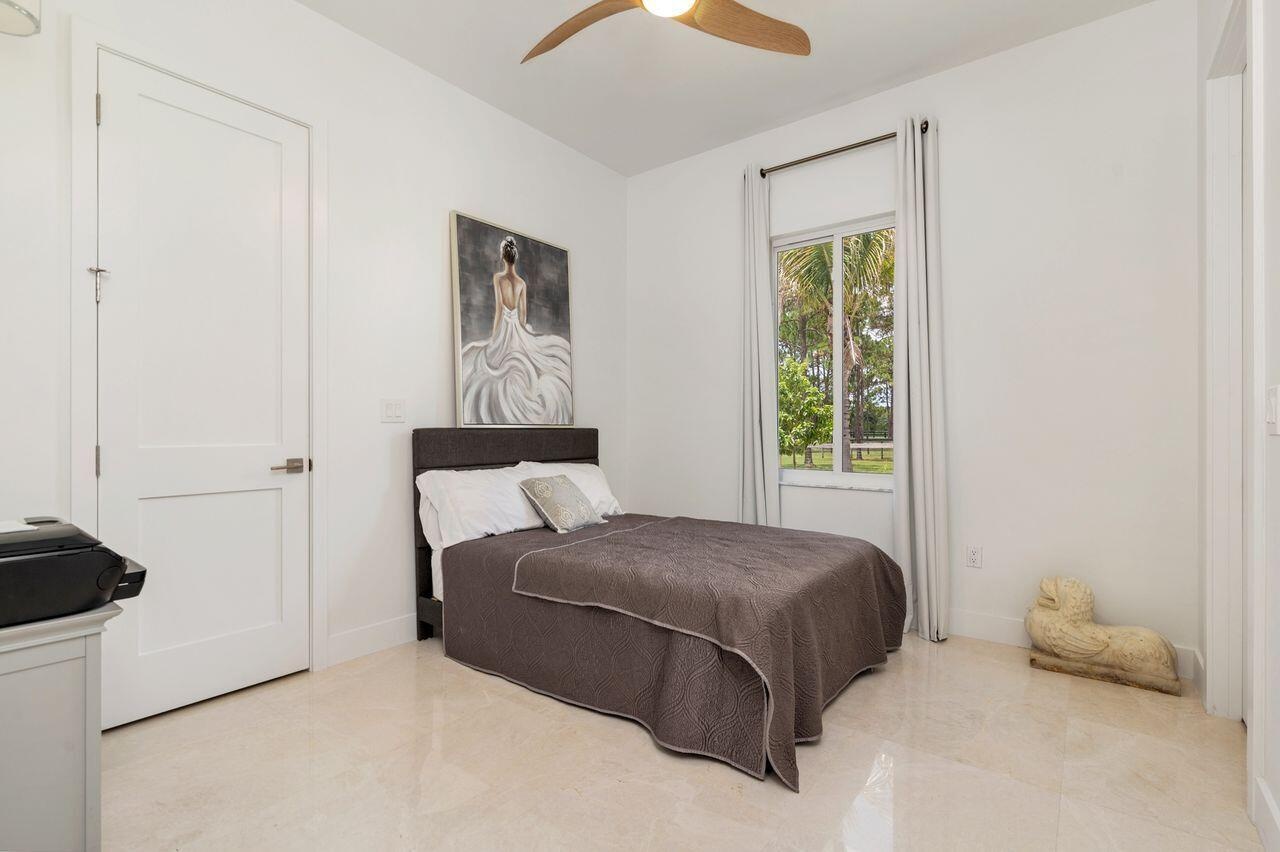 Light-filled guest bedroom featuring marble flooring, a modern ceiling fan, and a large window with outdoor landscaping visible