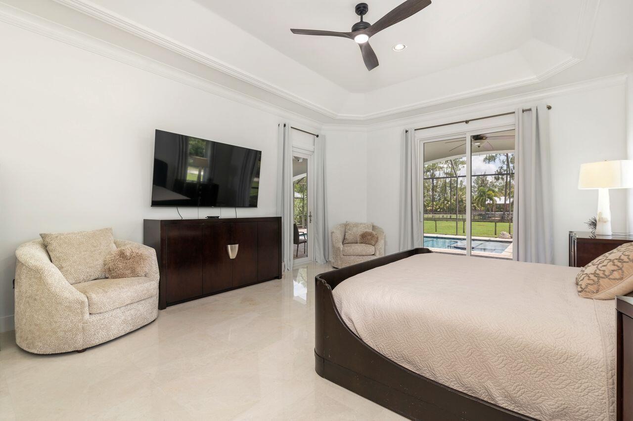 Spacious room featuring marble flooring, a tray ceiling with a dark-toned ceiling fan, and sliding glass doors opening to an exterior patio and pool a