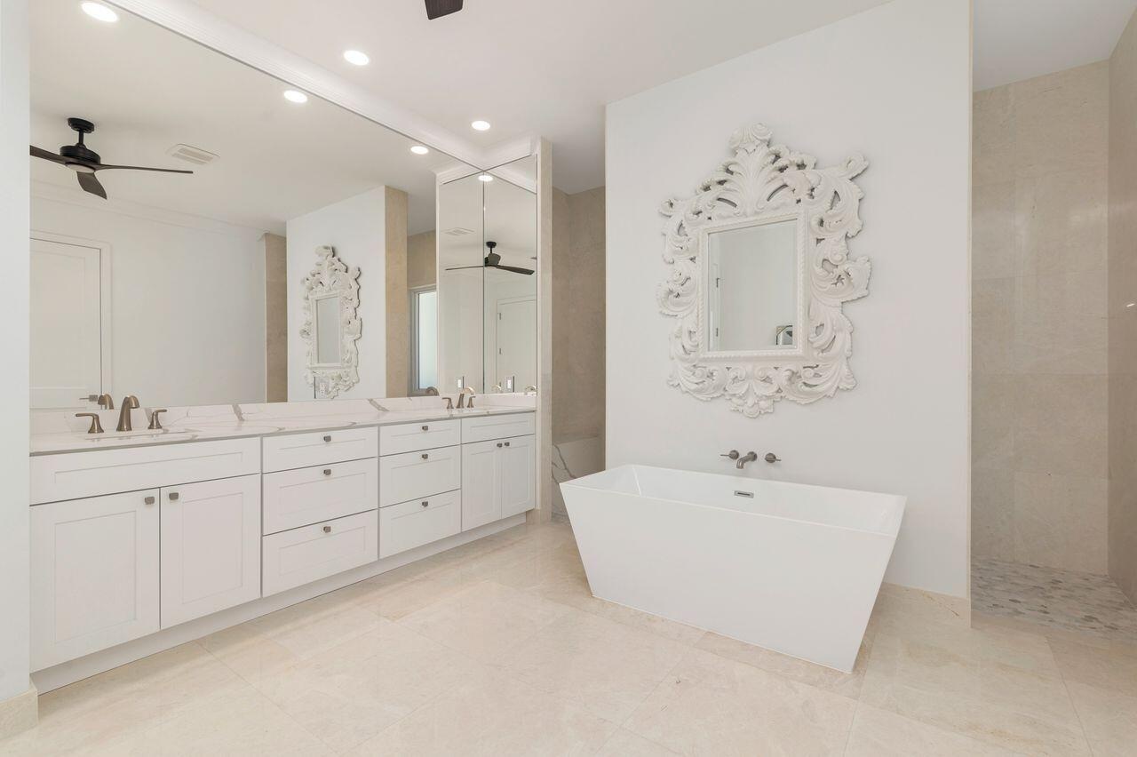 Spacious bathroom featuring a dual vanity with white cabinetry and light-toned countertops, a freestanding white soaking tub, and a glass-enclosed sho