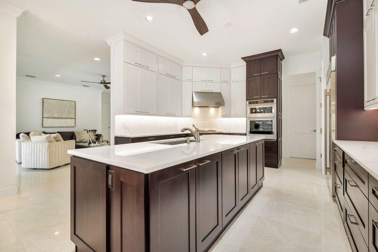 Gourmet kitchen featuring a large central island with integrated sink, two-tone cabinetry, built-in stainless steel appliances, and under-cabinet ligh