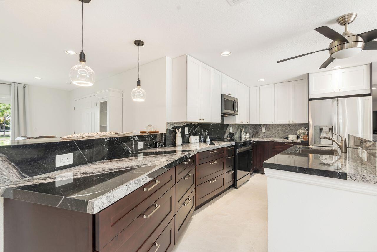Gourmet kitchen featuring dark wood cabinetry, white upper cabinets, stainless steel appliances, and contrasting dark countertops with a white vein pa