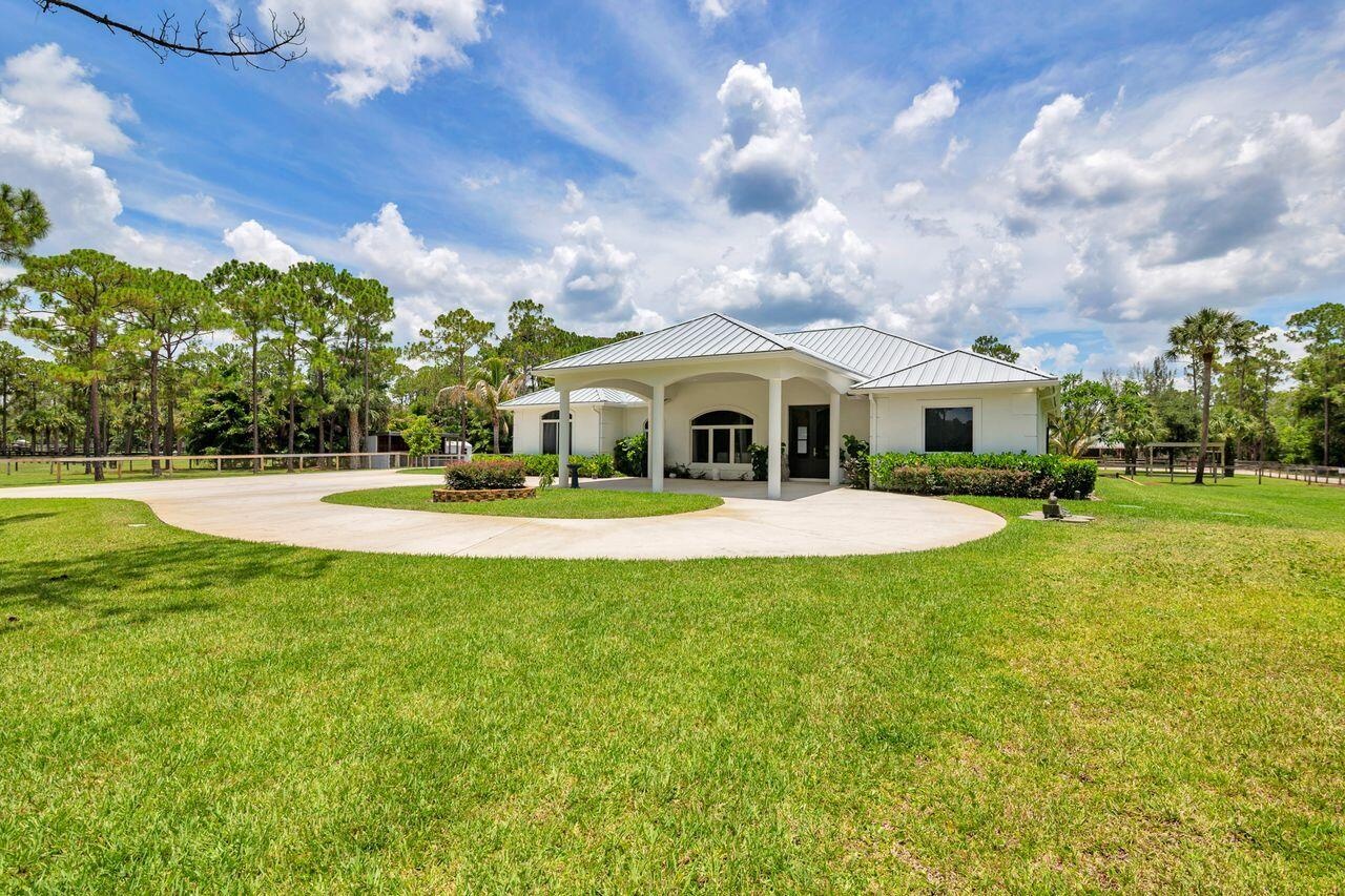 Spacious property featuring a white exterior residence with a covered entryway, a circular driveway, mature landscaping, and a surrounding privacy fen