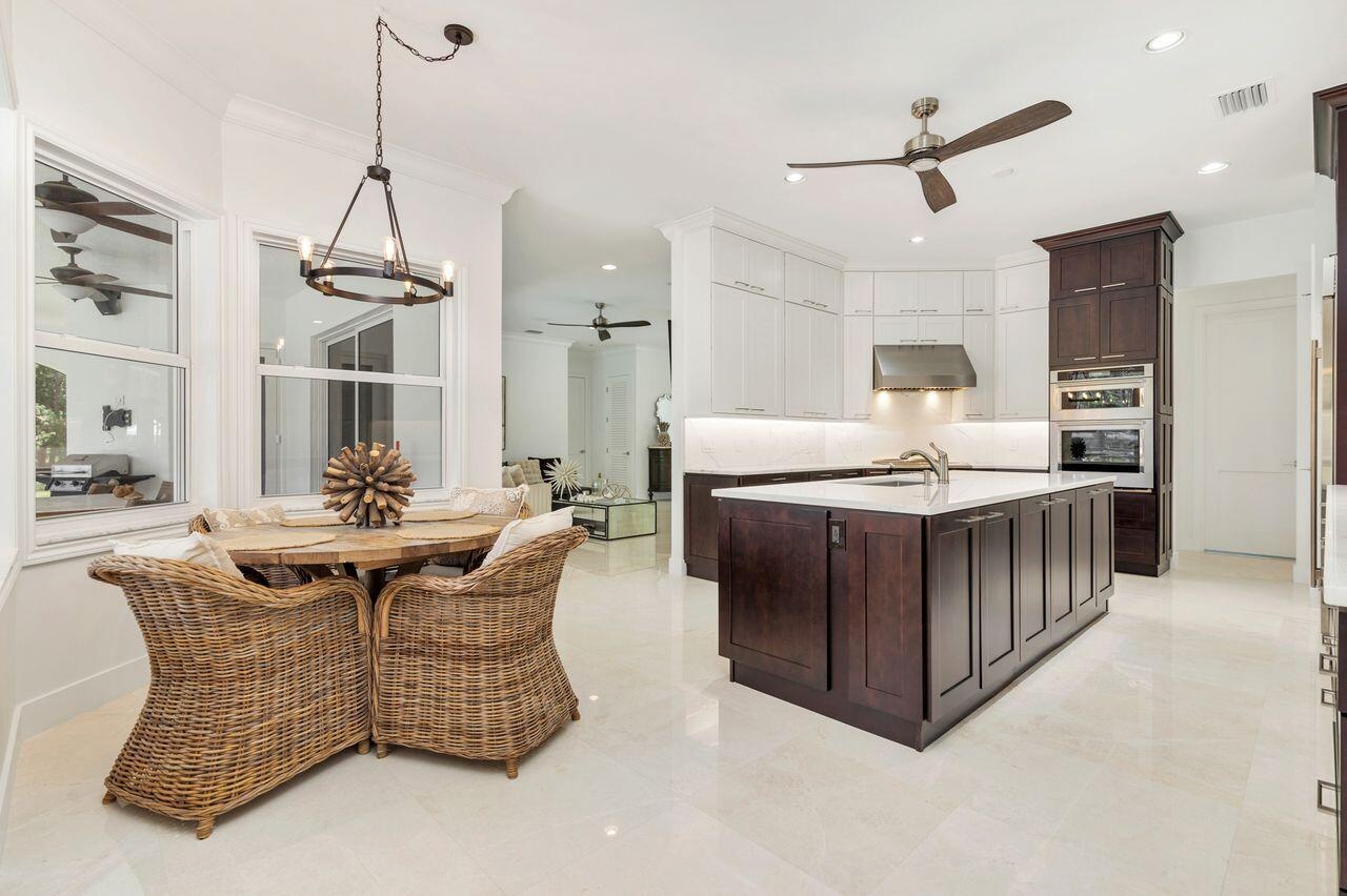 Modern kitchen featuring a large central island with a sink, white upper cabinetry, rich dark wood lower cabinetry, and built-in stainless steel appli