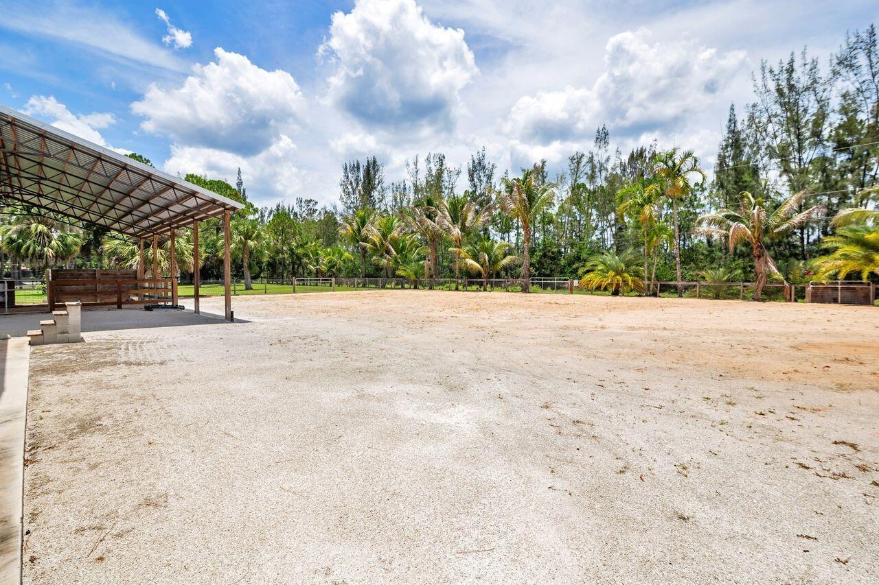 Expansive outdoor arena featuring a sand surface, perimeter fencing, and mature tropical landscaping