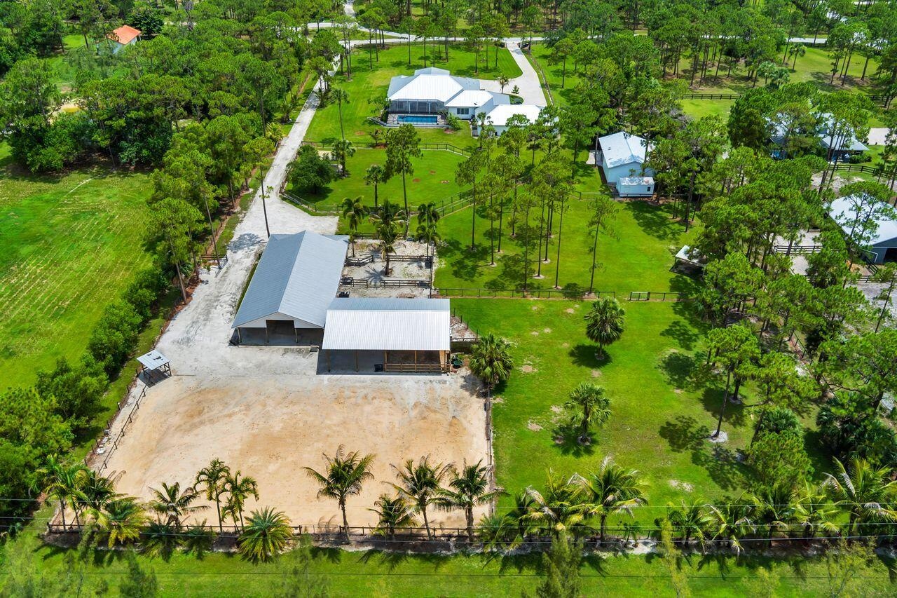 Expansive property featuring a main residence with a swimming pool, two metal-roofed outbuildings, a large equestrian arena, and mature trees with man