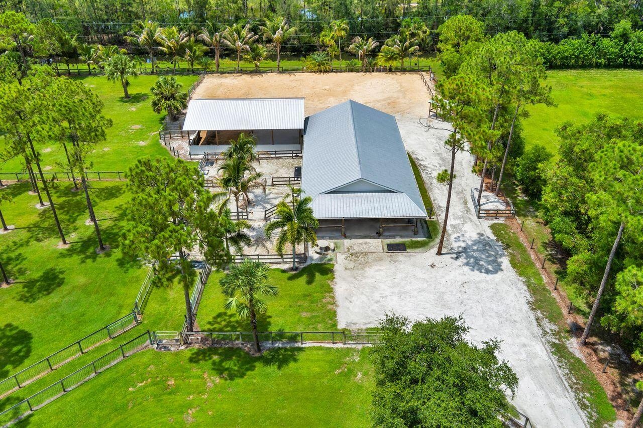 Expansive equestrian facility featuring two large structures with metal roofs and a sand arena