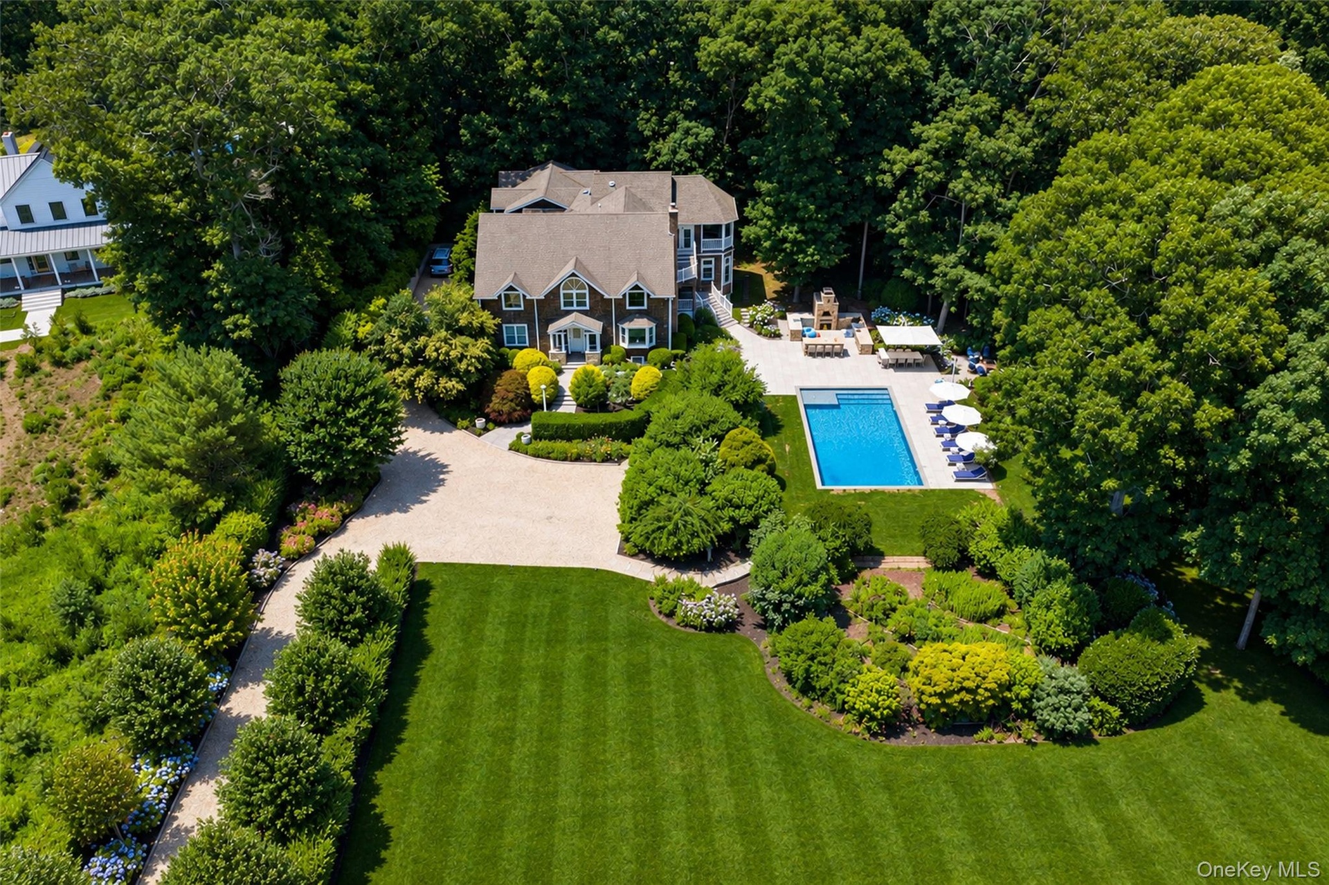 Expansive property featuring a large swimming pool, an outdoor hardscaping area, mature landscaping, a paved circular driveway, and a multi-story exte