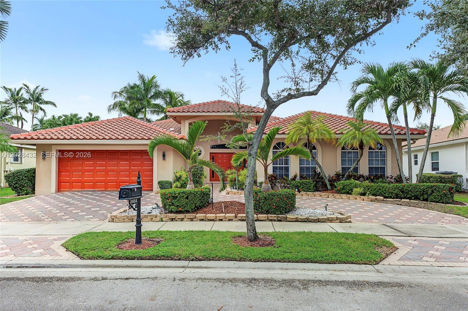 Stucco exterior featuring a multi-gabled tile roof, arched windows, and an expansive paved driveway