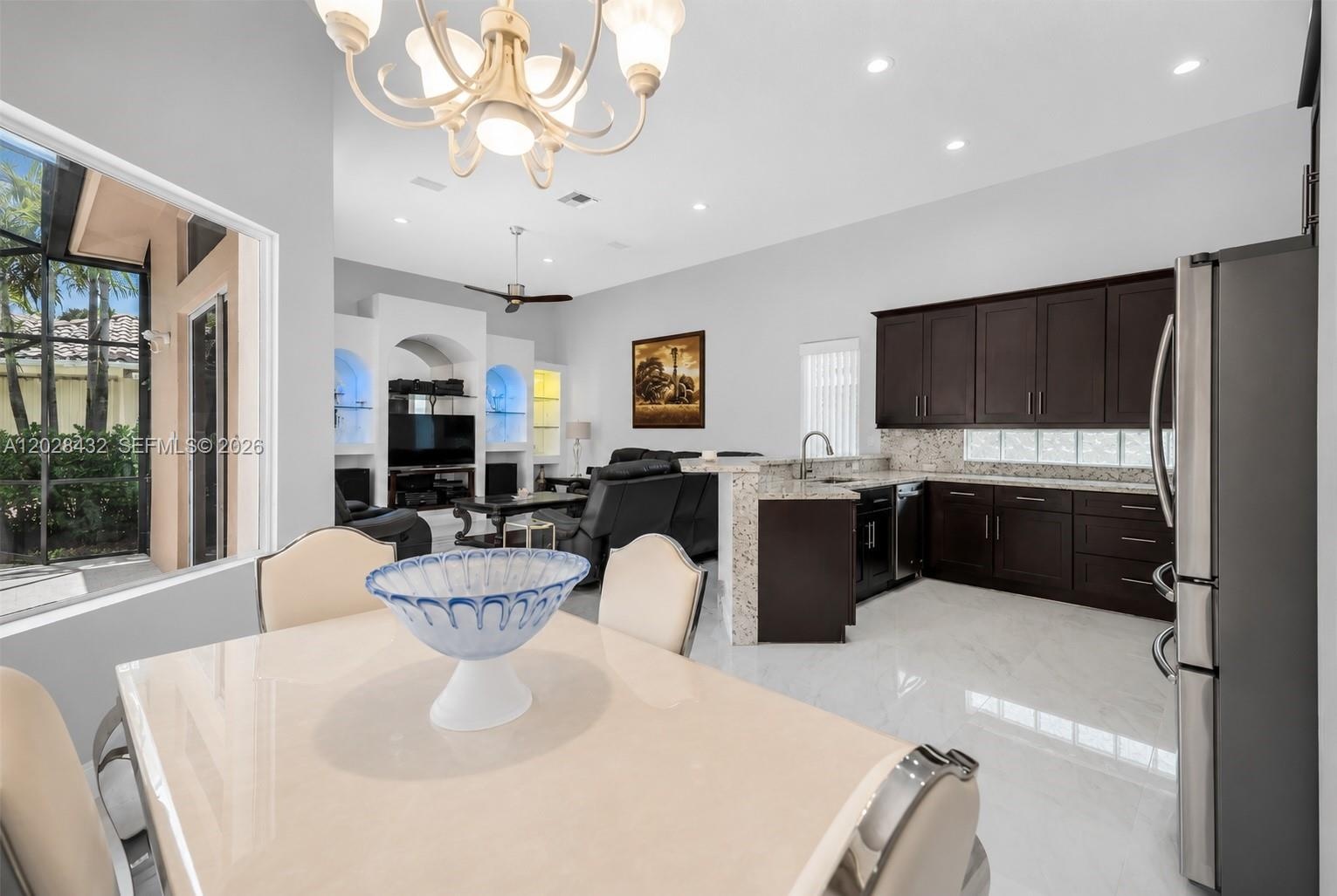 Open-concept space featuring polished stone-finish flooring, vaulted ceilings, expansive sliding glass doors, and a built-in stainless steel refrigera