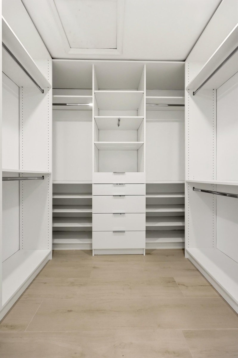 The custom walk-in closet is thoughtfully designed with extensive built-in storage, adjustable shelving, multiple hanging areas, and dedicated drawer 