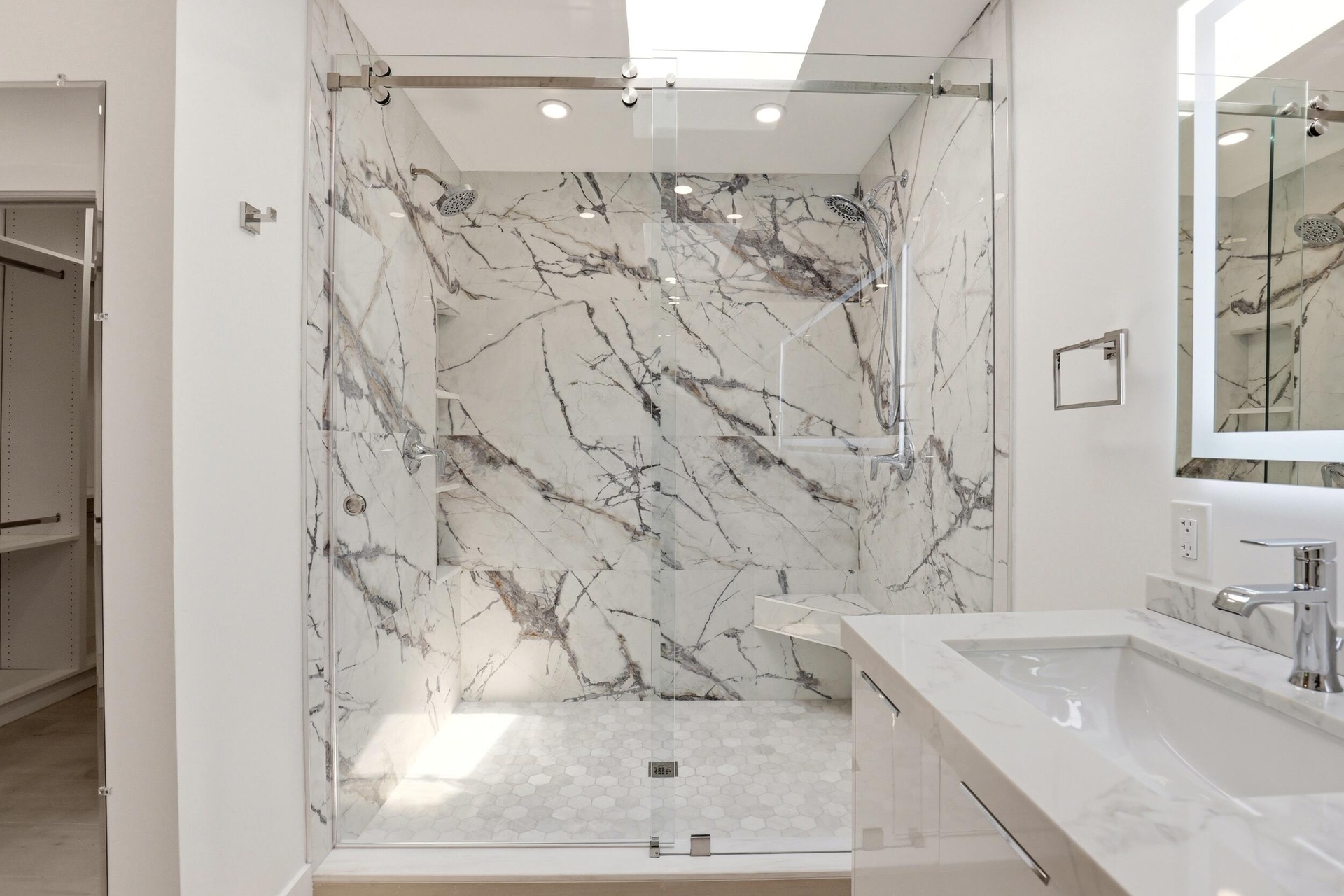 The spa-inspired primary bath showcases a sleek floating dual-sink vanity with quartz countertops, an illuminated designer mirror, and a stunning over
