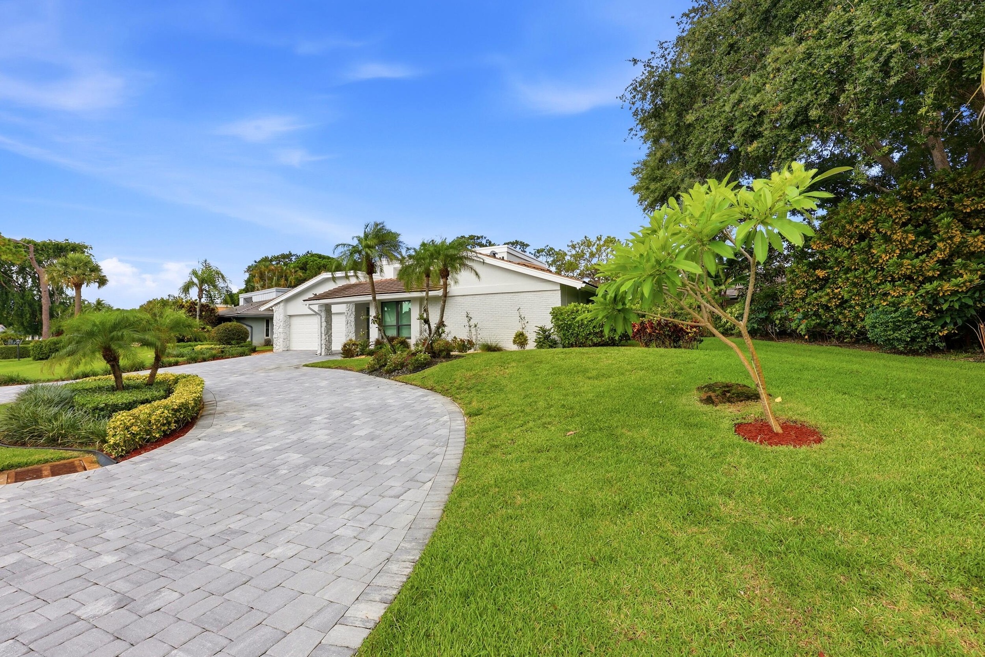 A striking first impression begins with a sweeping paver driveway, lush tropical landscaping, and timeless architectural details that set this home ap