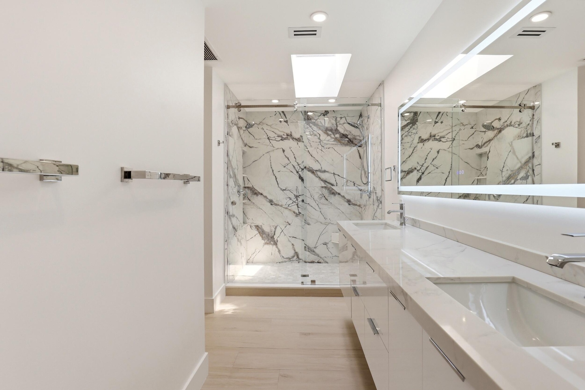 The spa-inspired primary bath showcases a sleek floating dual-sink vanity with quartz countertops, an illuminated designer mirror, and a stunning over