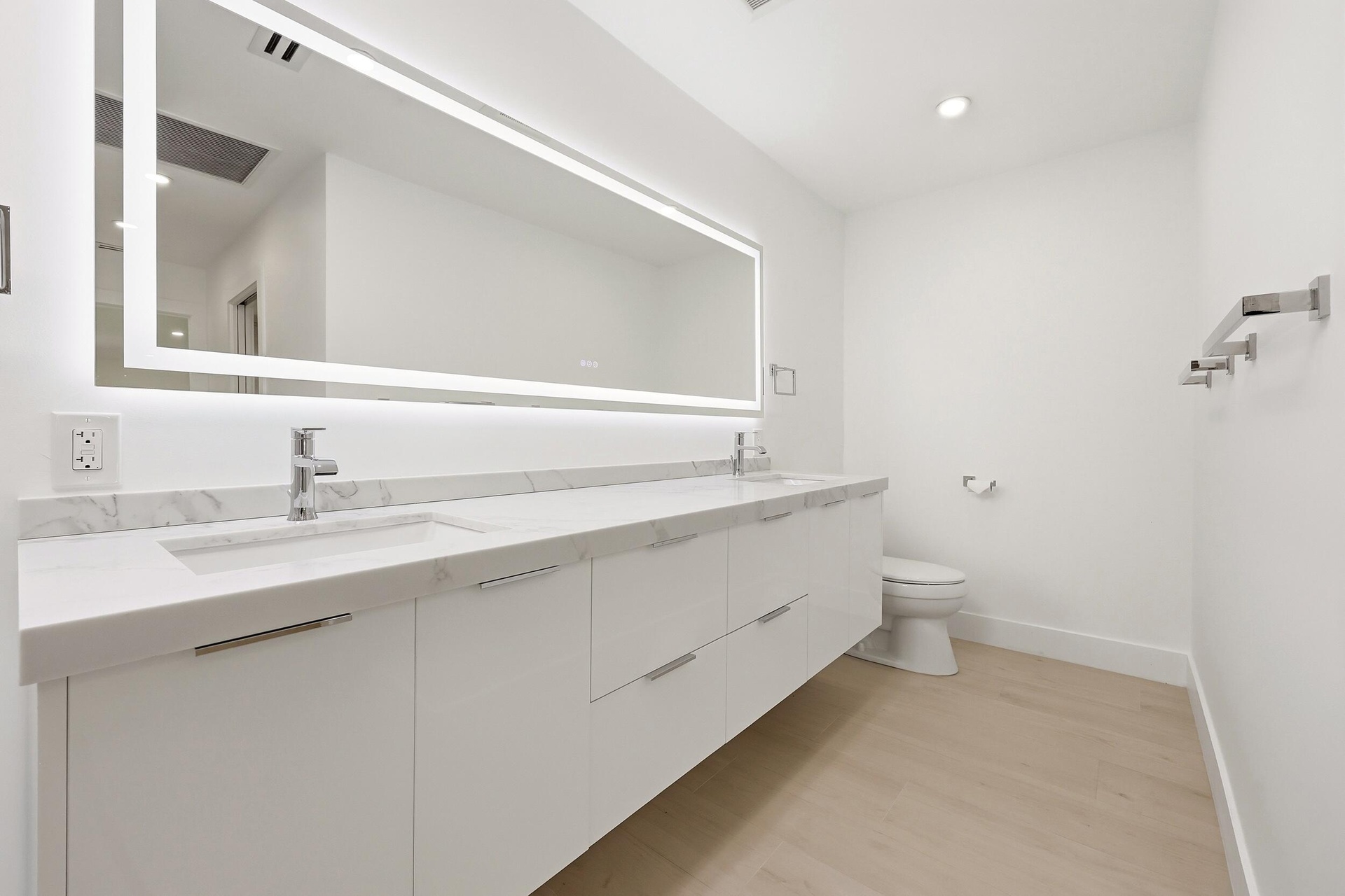 The spa-inspired primary bath showcases a sleek floating dual-sink vanity with quartz countertops, an illuminated designer mirror, and a stunning over