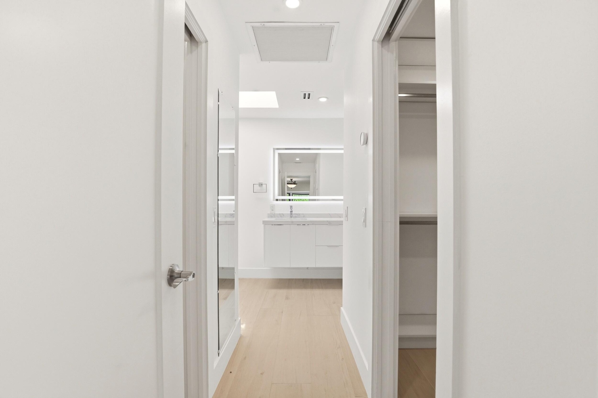 A thoughtfully designed hallway creates a seamless transition from the primary suite to the luxurious ensuite bath, offering a glimpse of the custom h