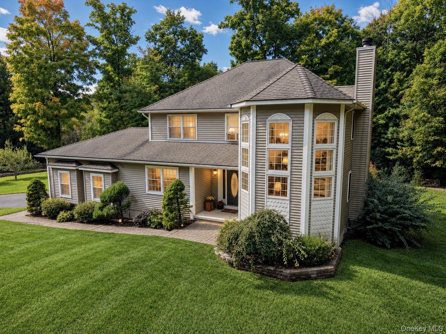 Siding exterior with a prominent architectural turret featuring stacked arched windows, a  chimney, and a paved walkway leading to the entry with land
