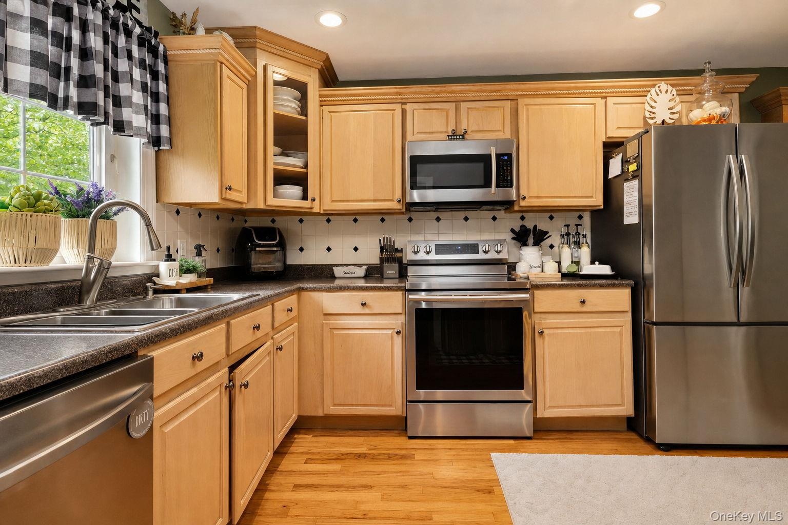 Natural wood cabinetry with crown molding, recessed lighting, stainless steel appliances, speckled countertops, a double-basin sink with a gooseneck f