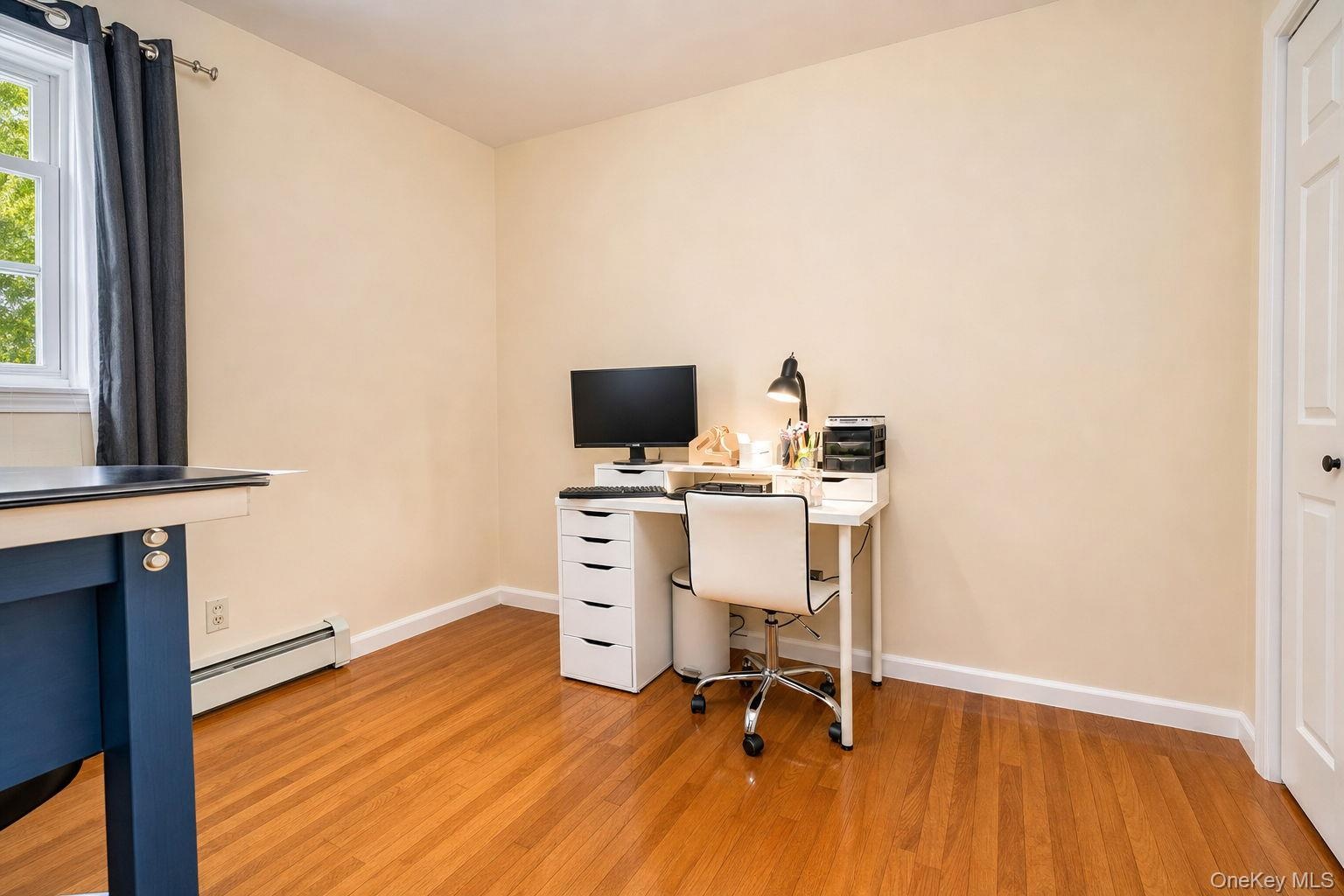 Hardwood flooring, painted walls, white trim, and a window with natural light used as an office