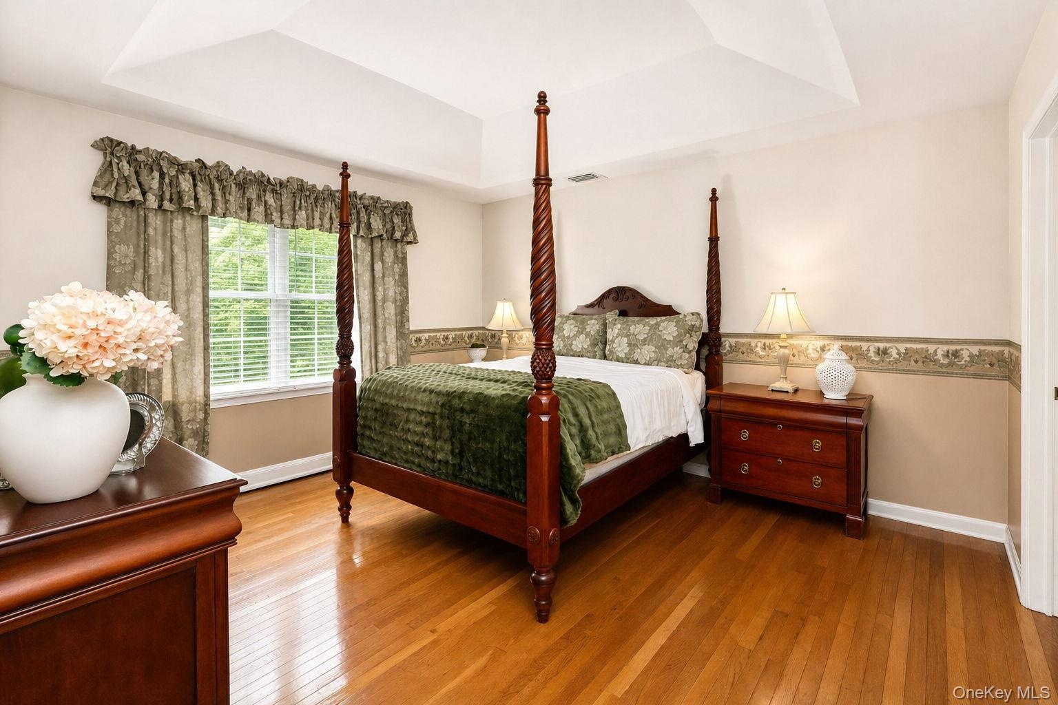Hardwood flooring, tray ceiling, chair rail, and a bright window with blinds