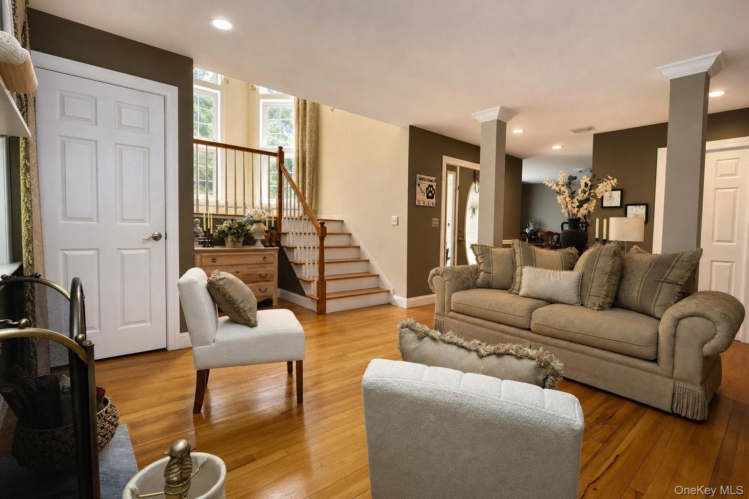 Hardwood flooring, painted interior doors, recessed lighting, white trim, decorative columns, and a wooden staircase with balusters