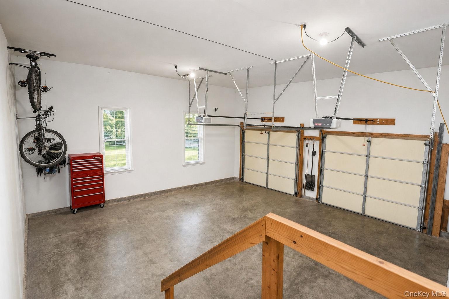 Two garage doors with openers,  concrete flooring, two windows, and overhead lighting