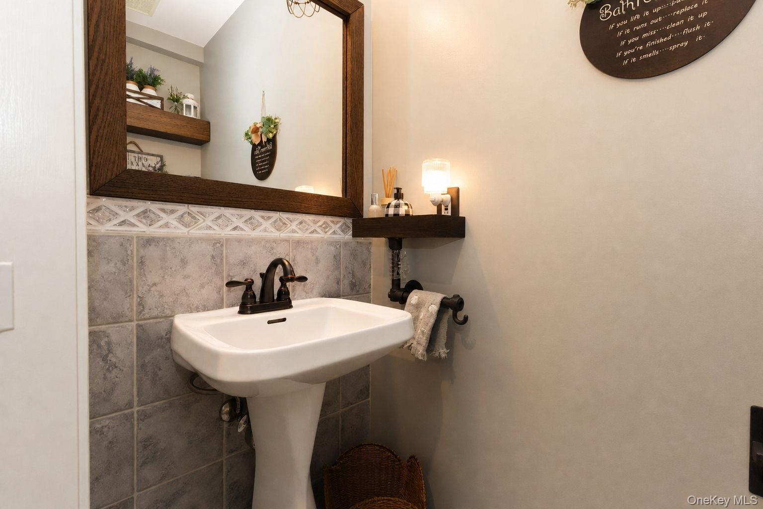 1/2 bath with pedestal sink with dark bronze faucet, tile wainscoting with decorative border, and a wood-framed mirror