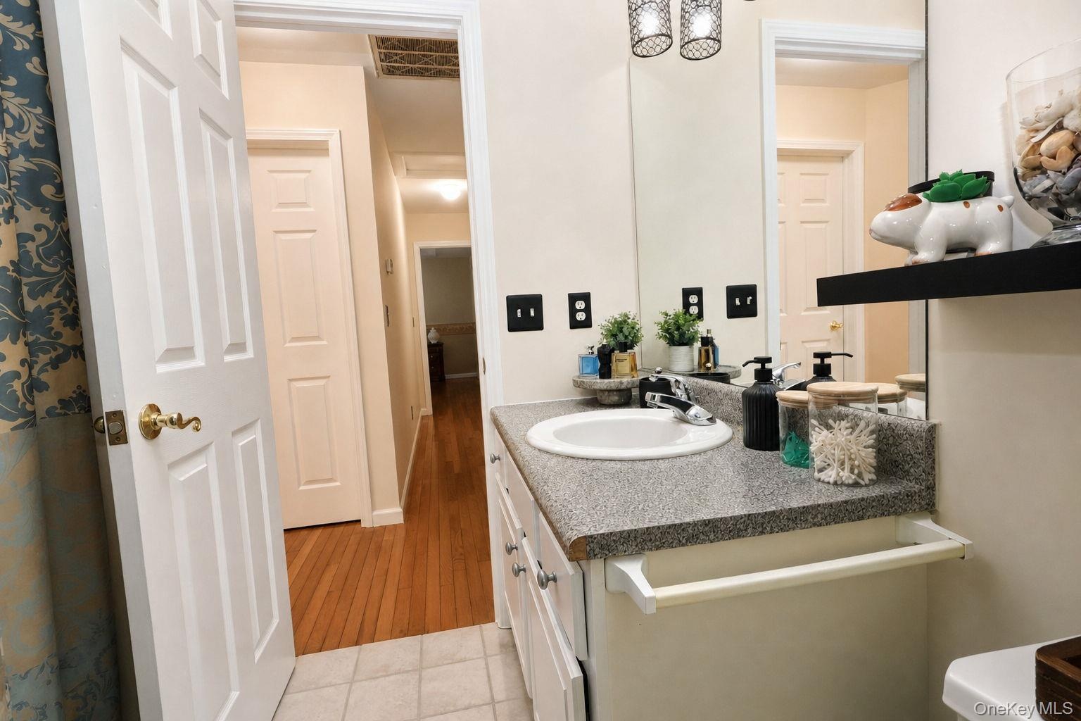 Vanity with integrated sink and speckled countertop, large wall-mounted mirror, overhead lighting fixture and a tub/shower