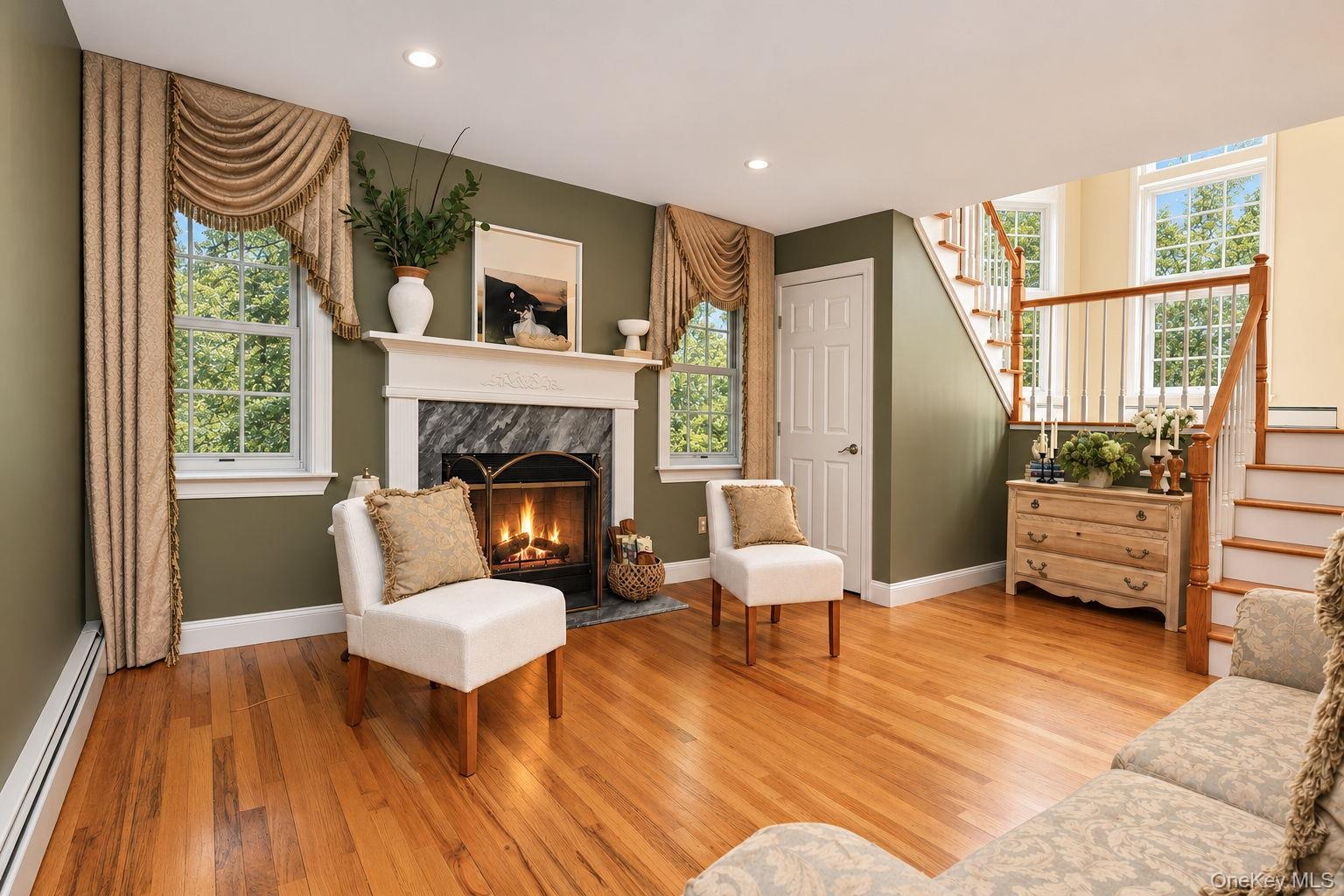 Hardwood flooring, fireplace with stone surround and mantel, multiple windows, and a staircase with wood railing