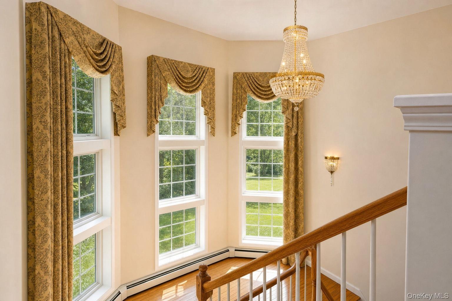 Hardwood flooring with a bay window arrangement, accented by a crystal chandelier and an ornate sconce
