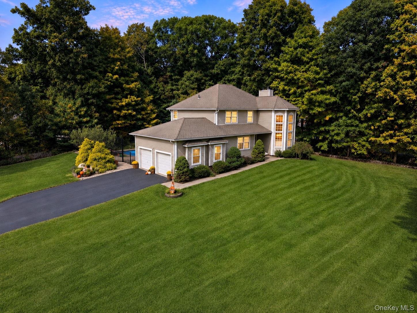 Traditional-style exterior with a paved driveway, attached 2 car garage, manicured lawn, and mature trees